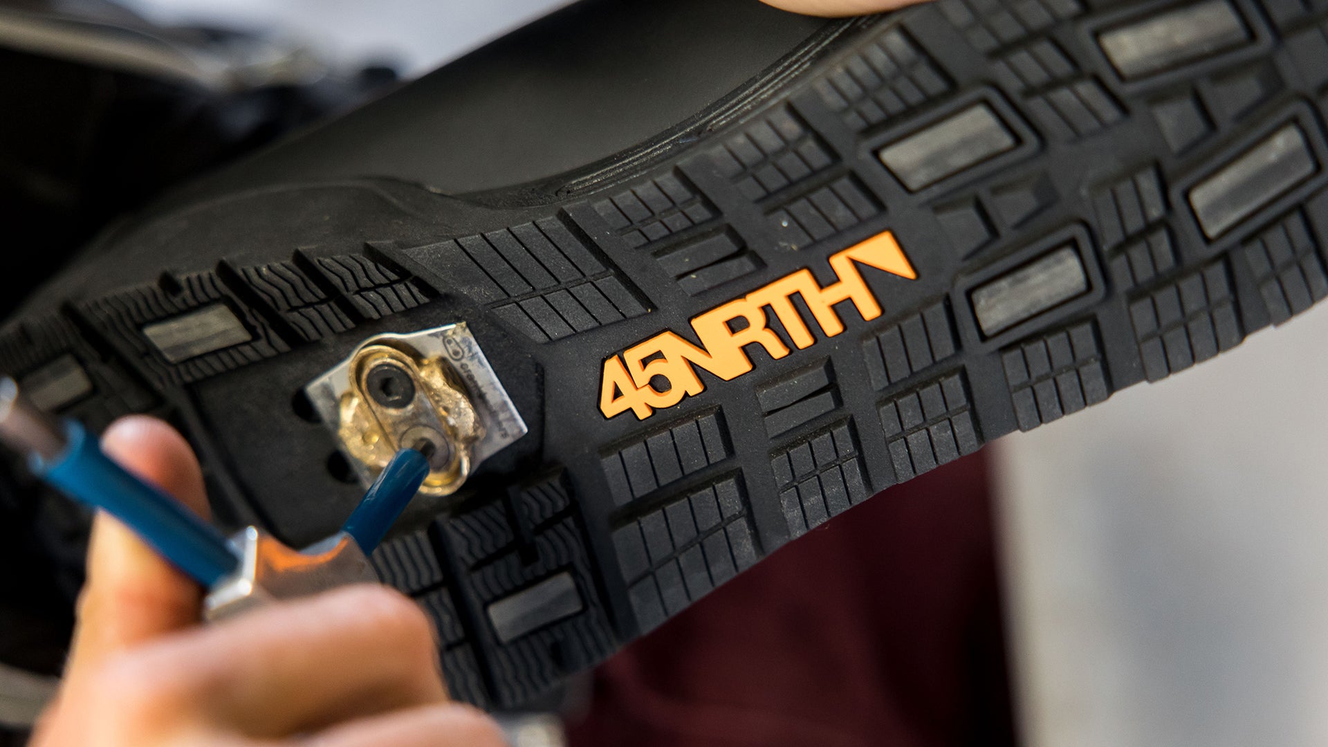 Close-up on person tightening cleat bolts on bottom of 45NRTH boot