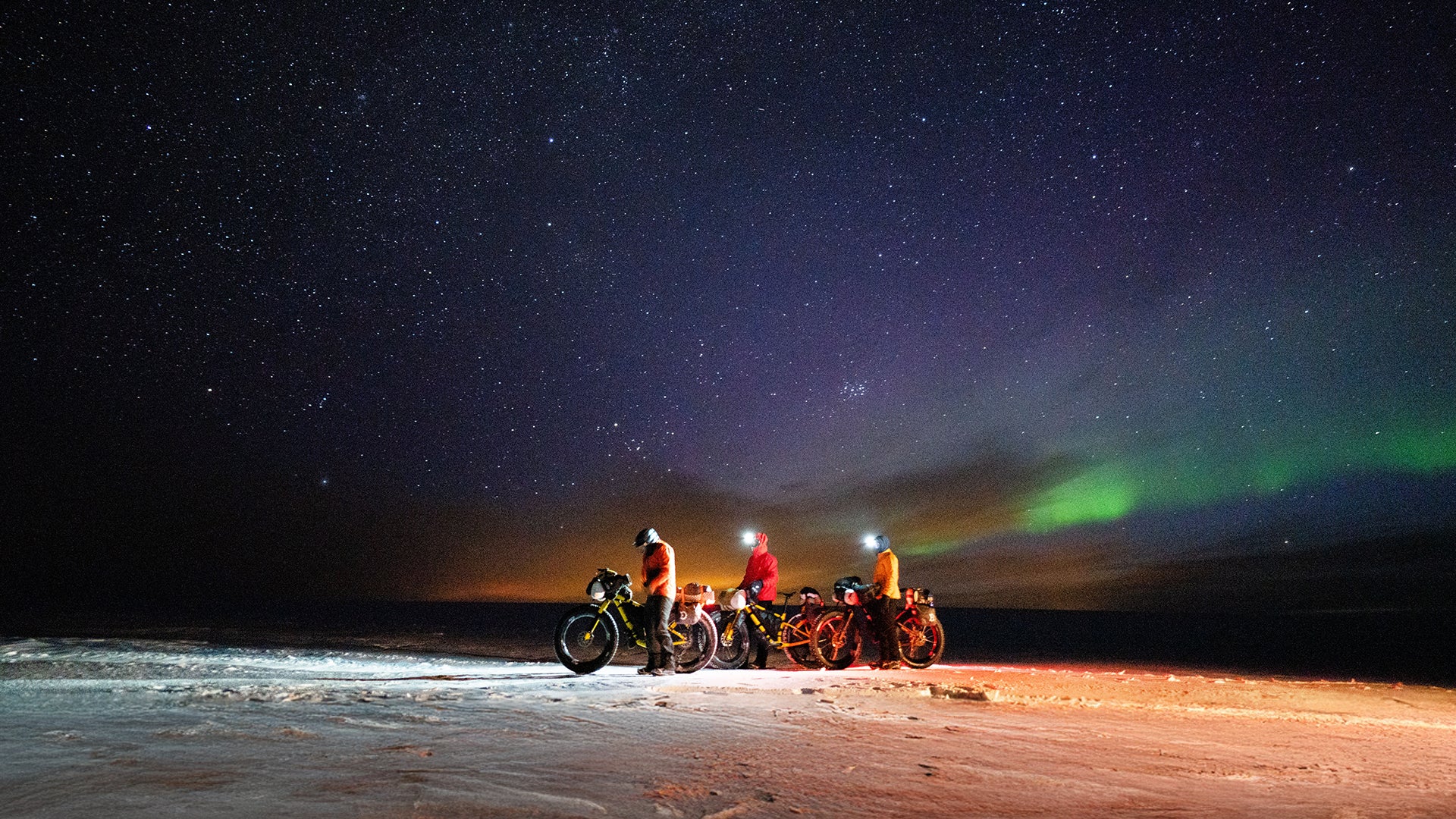 Three fat bikers stopped at night on clear night with stars and Northern Lights in background