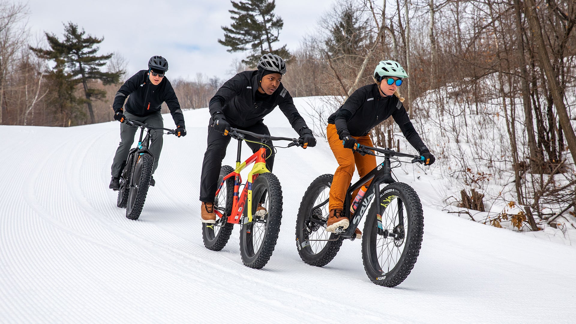 Three cyclists riding snowy groomed trail on fat bikes with studded fat bike tires