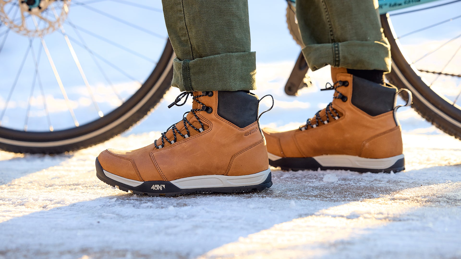 Close-up of cyclist wearing 45NRTH Boots on snow and ice standing next to bike